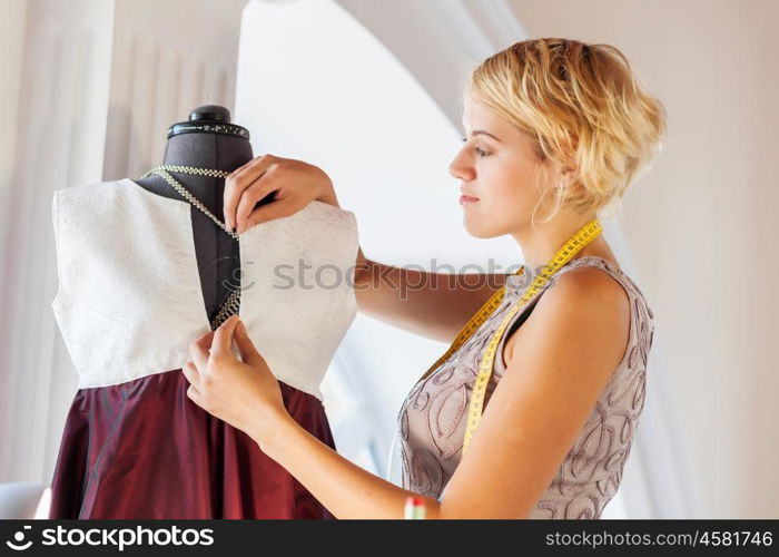 At tailors studio. Pretty dressmaker at work pinning dress on dummy