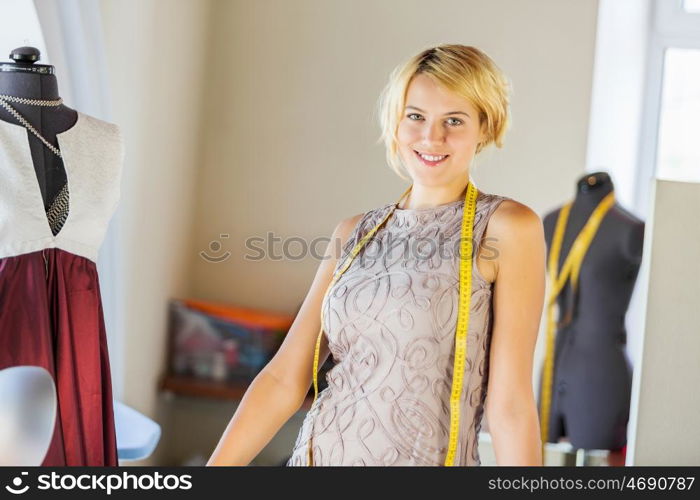 At tailors studio. Pretty dressmaker at work pinning dress on dummy