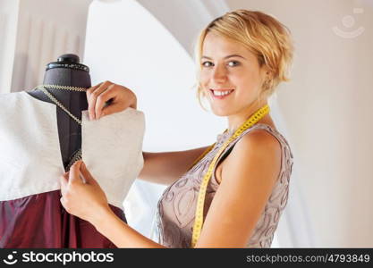 At tailors studio. Pretty dressmaker at work pinning dress on dummy