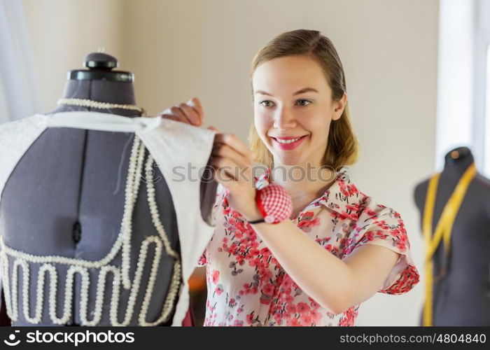 At tailors studio. Pretty dressmaker at work pinning dress on dummy