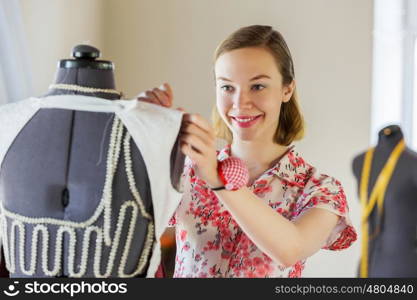 At tailors studio. Pretty dressmaker at work pinning dress on dummy