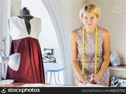 At tailors studio. Pretty dressmaker at work pinning dress on dummy