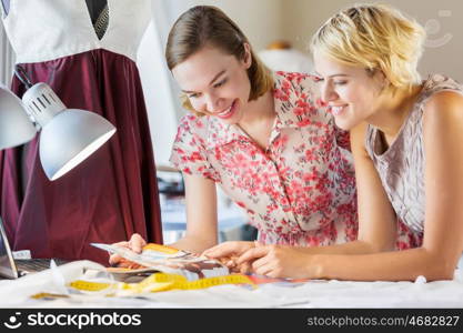 At tailors studio. Two attractive women at dressmakers choosing design