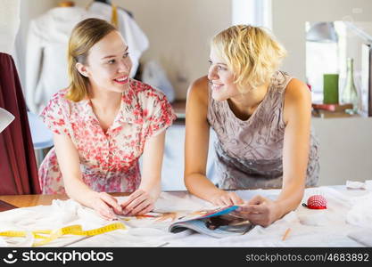 At tailors studio. Two attractive women at dressmakers choosing design