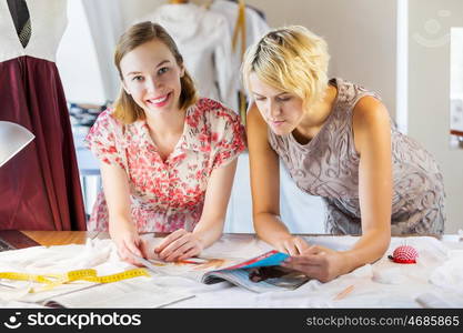 At tailors studio. Two attractive women at dressmakers choosing design