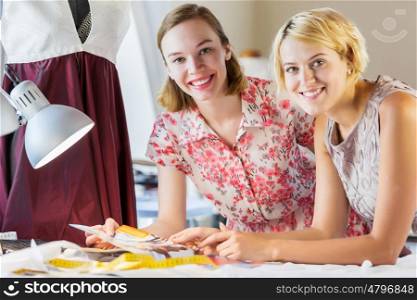 At tailors studio. Two attractive women at dressmakers choosing design