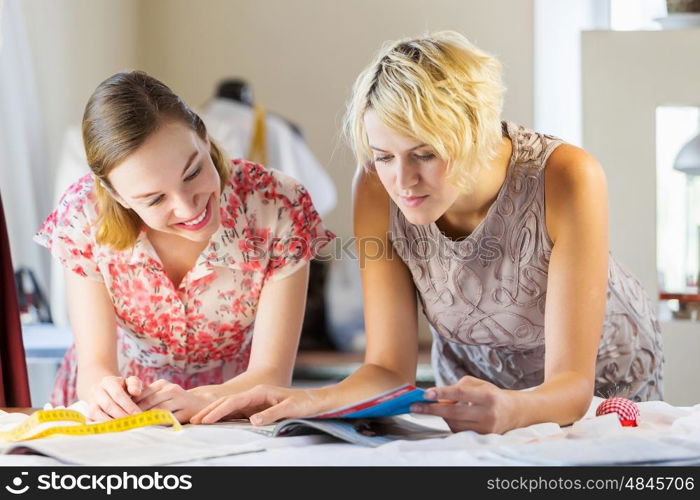 At tailors studio. Two attractive women at dressmakers choosing design