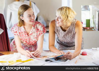 At tailors studio. Two attractive women at dressmakers choosing design