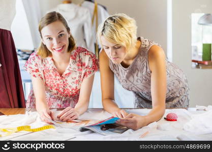 At tailors studio. Two attractive women at dressmakers choosing design