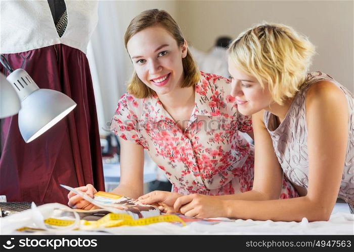 At tailors studio. Two attractive women at dressmakers choosing design