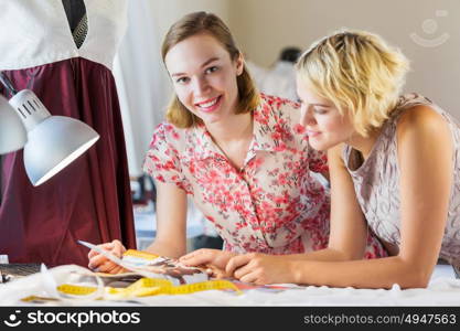 At tailors studio. Two attractive women at dressmakers choosing design