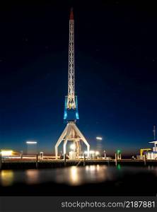 At the dock of the bay a high up crane against a blue starry sky and the red orange colors of the setting sun. Night photography in Harlingen harbor in the north of Dutch along the Wadden Sea and the North Sea. Beautifully illuminated industrial ship crane on the dock of a port