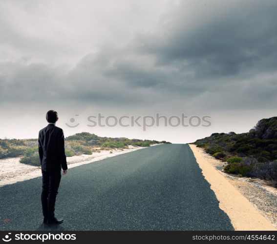 At the start of long way. Back view of businessman standing on road and looking far away