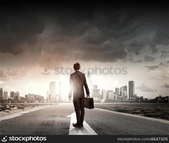 At the start of long way. Back view of businessman standing on road and looking far away