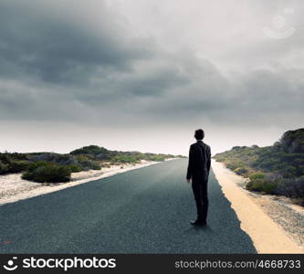 At the start of long way. Back view of businessman standing on road and looking far away