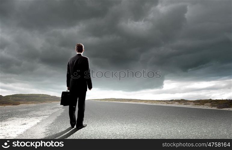 At the start of long way. Back view of businessman standing on road and looking far away