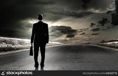 At the start of long way. Back view of businessman standing on road and looking far away