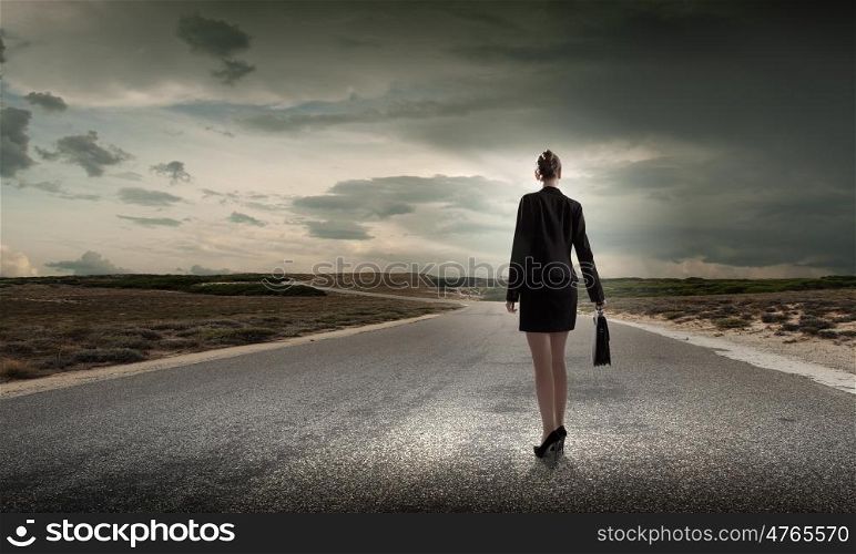 At the start of long way. Back view of businesswoman standing on road and looking far away