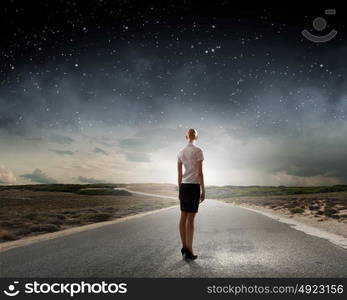 At the start of long way. Back view of businesswoman standing on road and looking far away