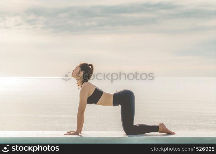 Athlete Attractive Asian woman relaxing in yoga Cat Cow Pose on the beach with beautiful sea,Feeling so comfortable and relax in holiday,Vacation of yoga on the beach,Yoga with Healthy Concept