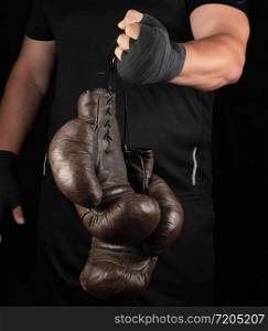 athlete in black clothes holds very old vintage leather black boxing gloves, low key