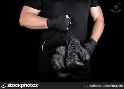 athlete in black clothes holds very old vintage leather black boxing gloves, low key