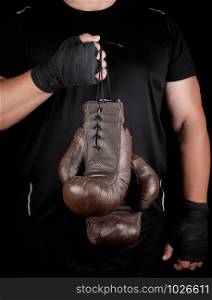 athlete in black clothes holds very old vintage leather brown boxing gloves, low key