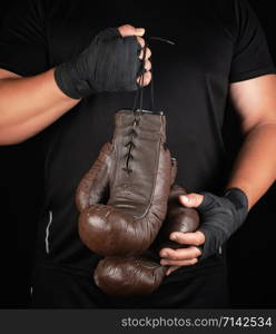 athlete in black clothes holds very old vintage leather brown boxing gloves, low key