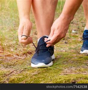 athlete in black uniform crouched and tying the laces on blue sneakers in the middle of the forest, concept of a healthy lifestyle and jogging