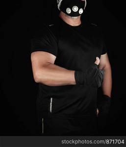 athlete in black uniform, training mask and hands wrapped in black bandage stands and shows a hand gesture like, black background