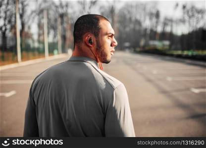 Athlete in headphones before jogging in park. Jogger on morning fitness workout. Runner in sportswear, fitness training outdoor. Athlete in headphones before jogging in park