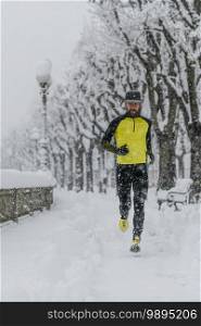 Athlete man runs on a city sidewalk during heavy snowfall