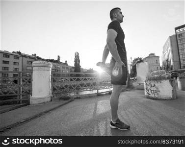 athlete man warming up and stretching while preparing for running on the city street at sunny morning