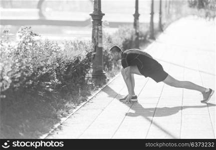athlete man warming up and stretching while preparing for running on the city street at sunny morning