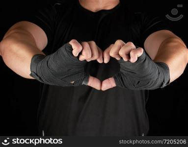 athlete shows the symbol of the heart, palm of a man is wrapped in a black sports bandage, black background