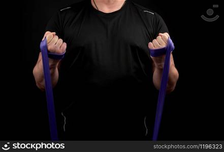 athlete with a muscular body in black clothes is doing physical exercises with purple rubber, low key