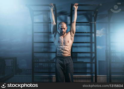 Athlete with muscular body training on horizontal bar in gym. Muscle man on workout. Athlete with muscular body training on bar