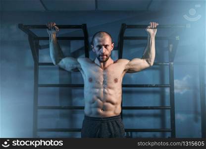 Athlete with muscular body training on horizontal bar in gym. Muscle man on workout