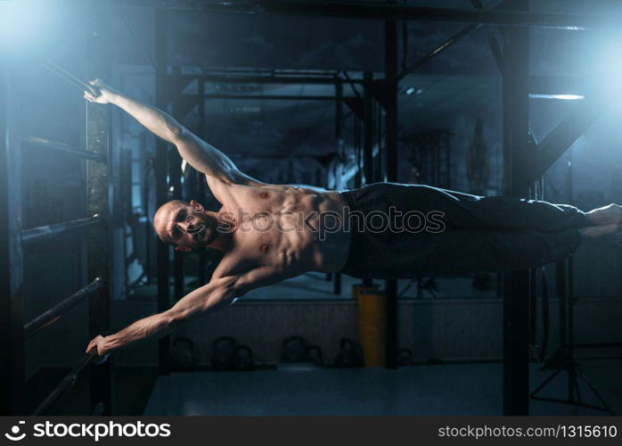 Athlete with muscular figure making efforts to preserve the horizontal balance on bar. Strong man on training