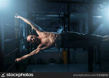 Athlete with muscular figure making efforts to preserve the horizontal balance on bar. Strong man on training