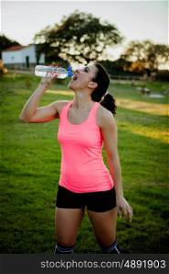 Athlete woman with sportswear drinking water in the field