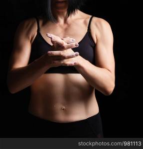athletic arms with veins and the muscular torso of a young girl with black hair, she rubs white magnesia into her skin, low key