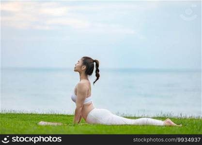 Athletic Asian young woman practice Cobra Pose on green grass and beach in Tropical island,Feeling comfortable and relax in holiday,Vacations Yoga Concept
