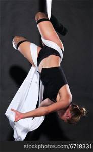 Athletic blonde aerialist suspended from white fabric