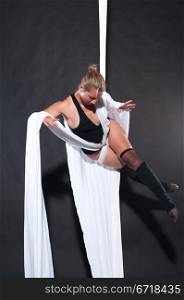 Athletic blonde aerialist suspended from white fabric