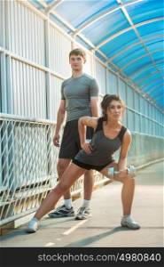 Athletic couple pumping up muscles with dumbbells outdoors in the city