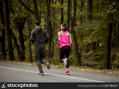 Athletic couple running together on the forest trail in autumn