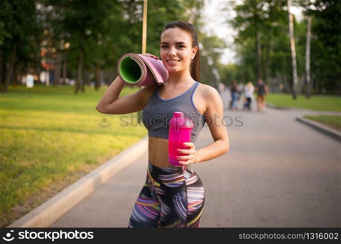 Athletic girl with sport bottle in summer park. Woman on morning workout. Athletic girl with sport bottle in summer park