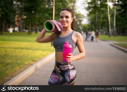 Athletic girl with sport bottle in summer park. Woman on morning workout. Athletic girl with sport bottle in summer park