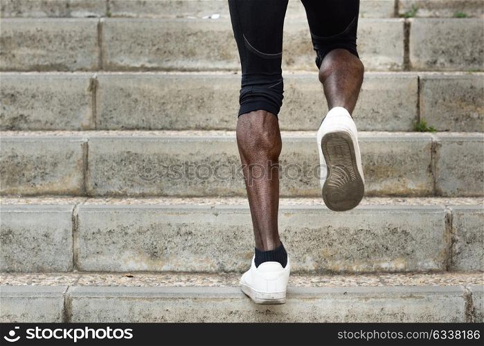 Athletic legs of black sport man with sharp muscles running on staircase steps. African male jogging in urban training workout.